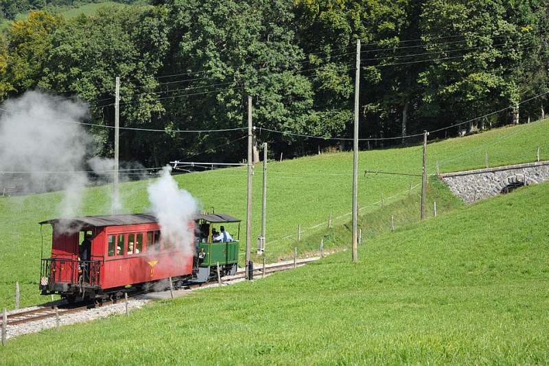 La locomotive à vapeur G 2/2 4 des anciennes Ferrovie e Tramvie Padane (Italie) circule ici sur le chemin de fer-musée Blonay-Chamby durant l’été 2011, avec un train de voyageurs descendant vers Blonay depuis Cornaux. Derrière elle se trouve une voiture voyageurs historique du chemin de fer Nyon–Saint-Cergue–Morez.